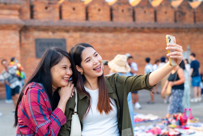 Happy Asian woman using smartphone taking selfie or vlogging during travel and shopping traditional street market in Chiang Mai city. People enjoy outdoor lifestyle travel Thailand on holiday vacation