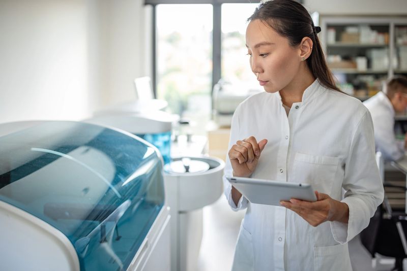 In a state-of-the-art laboratory, a focused scientist uses a tablet to interact with advanced equipment, showcasing modern tech integration in scientific fields.
