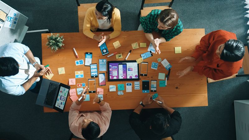 Top down view of business team writing idea on sticky note while planing for Ux Ui design for mobile phone interface. Group of creative designer working on wireframe prototype design. Convocation.