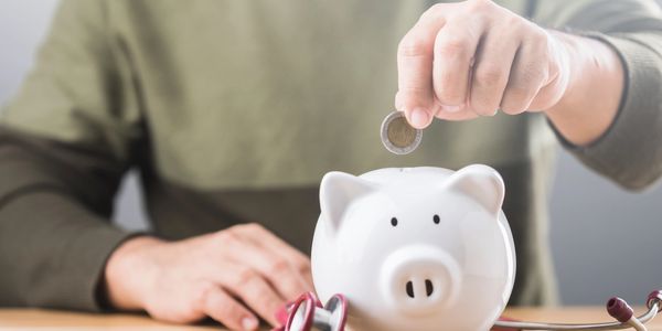 Person putting a coin into a piggy bank with a stethoscope nearby.
