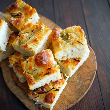 Fresh rosemary focaccia bread slices on a wooden board.