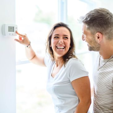 Happy couple adjusting home thermostat.