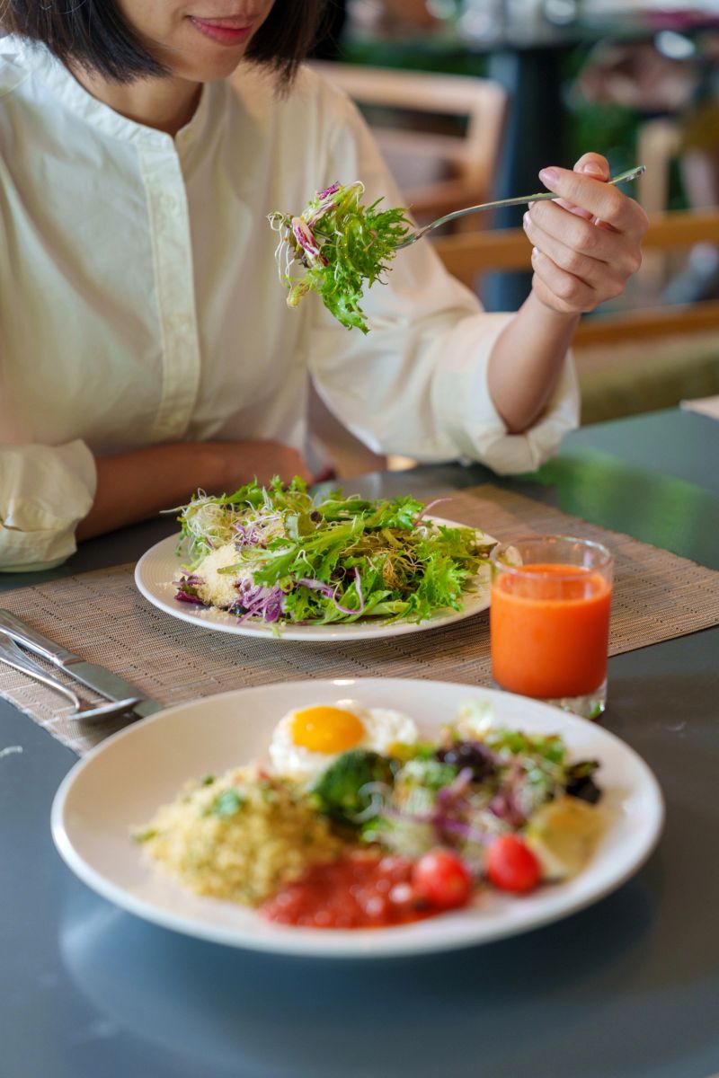 A wholesome plant-based meal served with couscous, a fried egg, fresh broccoli, salad, and a side of tomato sauce, complemented with a glass of refreshing orange juice. The colorful and nutrient-packed plate makes for a healthy, balanced meal perfect for any time of day.
