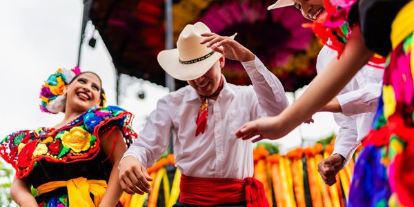 People joyfully dancing in colorful traditional Mexican attire at a festive outdoor event.