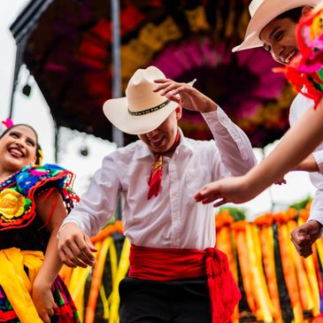 People joyfully dancing in colorful traditional Mexican attire at a festive outdoor event.