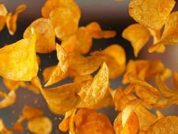 Close-up of crispy potato chips mid-air with seasoning.