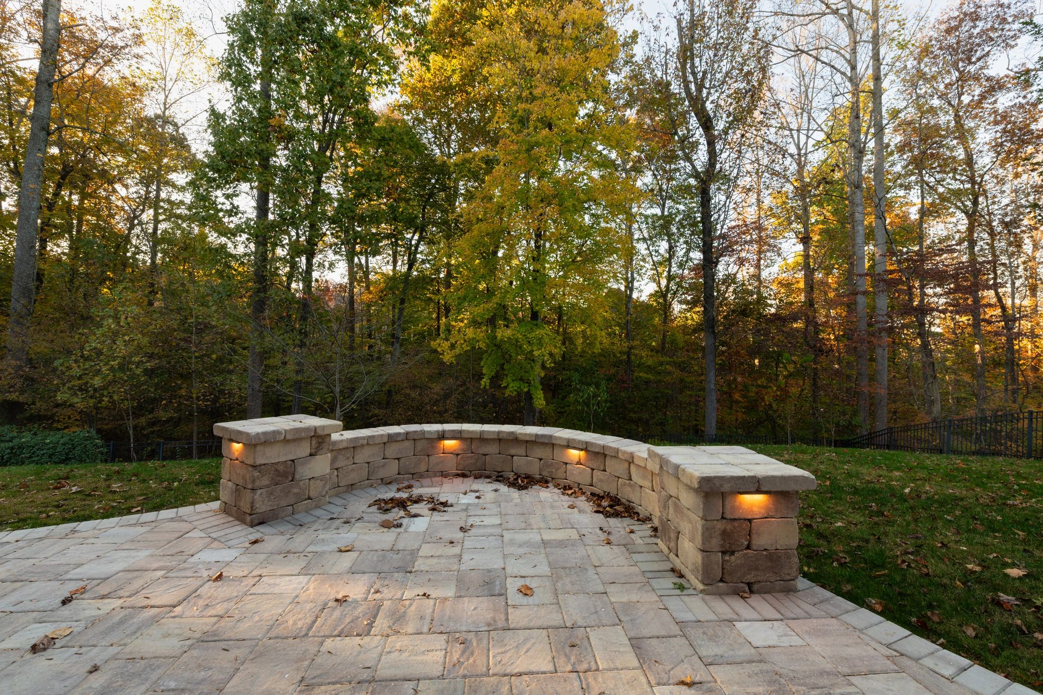 Curved stone bench with built-in lights in a forested backyard.
