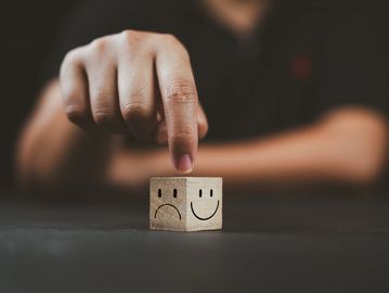 Hand flipping a wooden block from sad face to happy face.