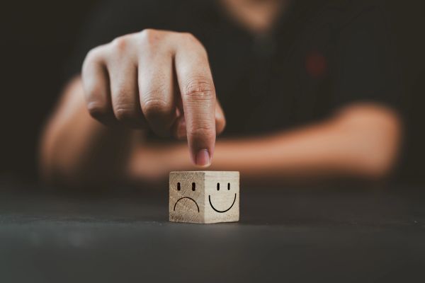 A dice with a smiling face and a sad face side on it, with a finger pointing to it in terms of menta