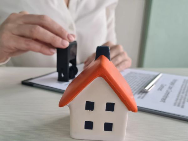 A person stamping a document behind a small house model on a desk.