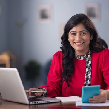 Smiling woman working on a laptop and holding a calculator.
