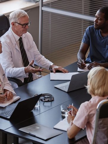 Medical professionals hold a discussion around a conference table with brain scans in the background.