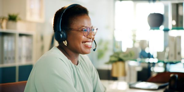 Smiling woman wearing headset and glasses in a bright office.