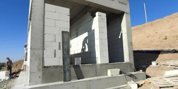 Partially constructed small concrete building with workers in bright daylight.