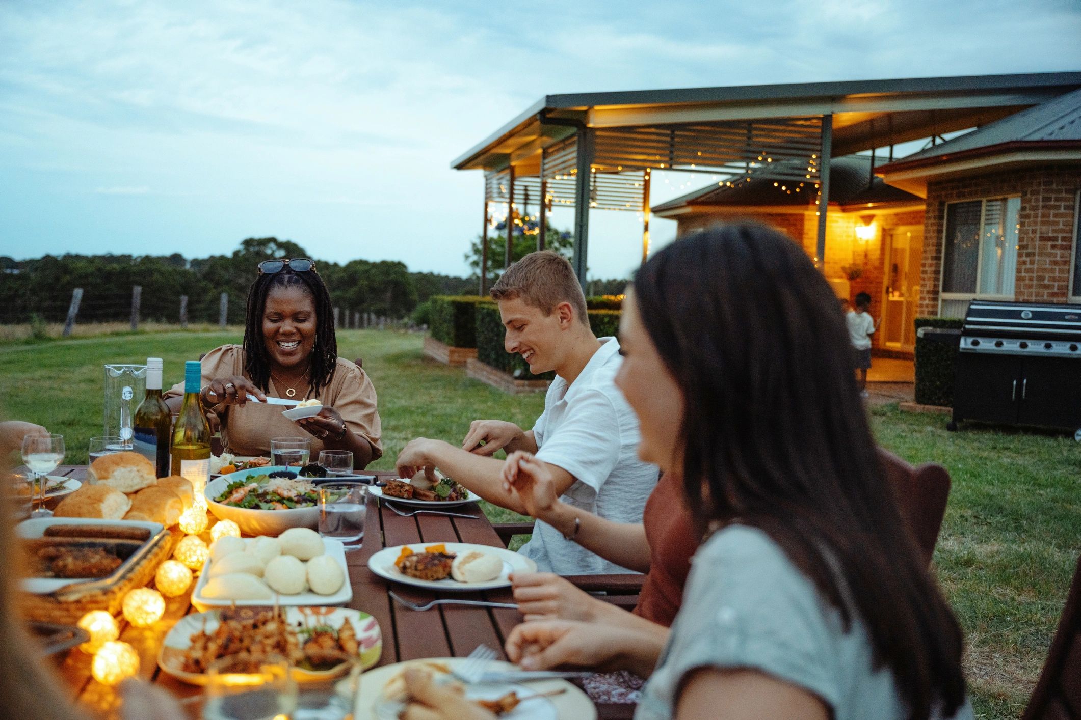 Friends enjoying a cozy outdoor dinner party with lights and delicious food.