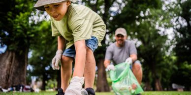 Child and adult cleaning up park, picking trash together.