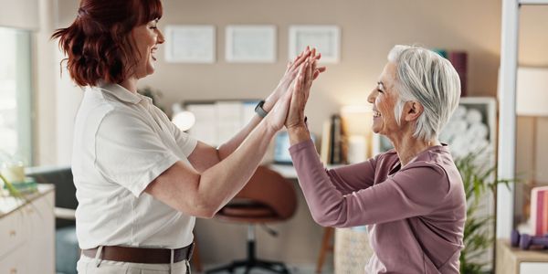 A joyful elderly woman and caregiver share a happy moment together indoors.