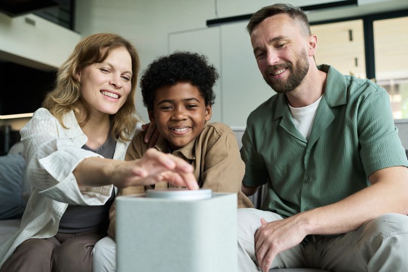 Family using interactive device while sitting together on couch, smiling and enjoying each other's company, showing close bond and happiness