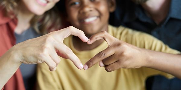 A diverse family forms a heart shape with their hands, smiling warmly.