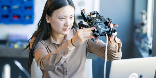 Woman examining a robotic device carefully in a tech workspace.
