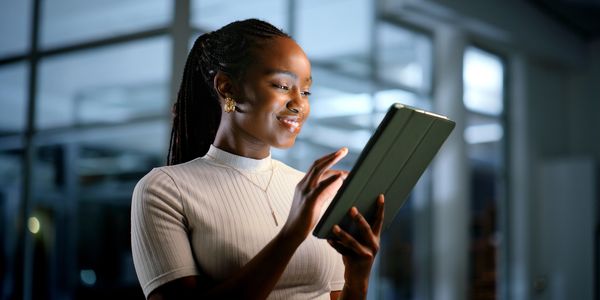 Smiling woman using a tablet indoors with soft lighting.