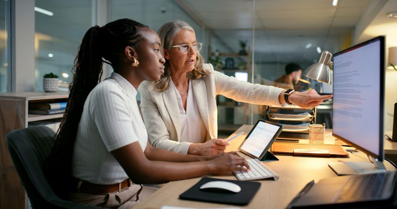 Business, people and computer with training in office to prepare accounting reports and finance filing system. Mentor, mature manager and helping intern accountant to track financial payments at desk