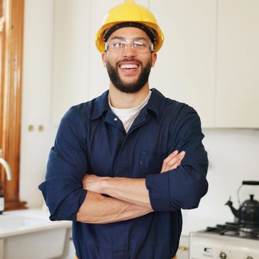Smiling handyman in safety gear standing confidently in a kitchen.