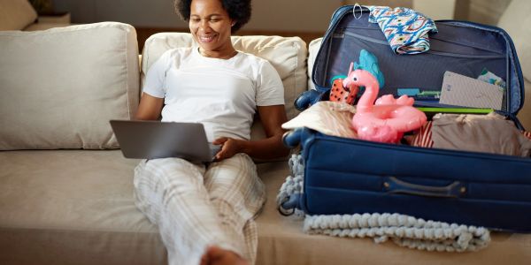 Woman sitting on couch using laptop next to a packed suitcase.