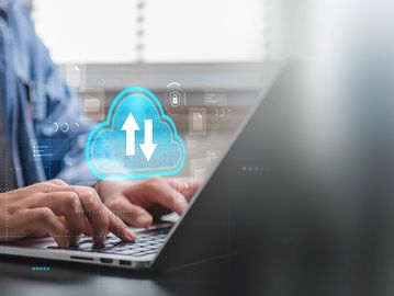 Person typing on laptop with digital cloud upload and download icons.