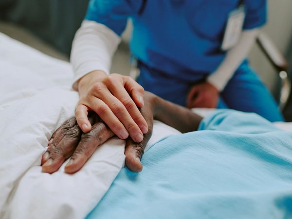 Nurse comforting a patient by holding their hand in a hospital bed.