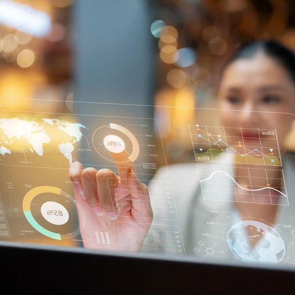 Woman interacting with futuristic transparent digital interface displaying global data and charts.