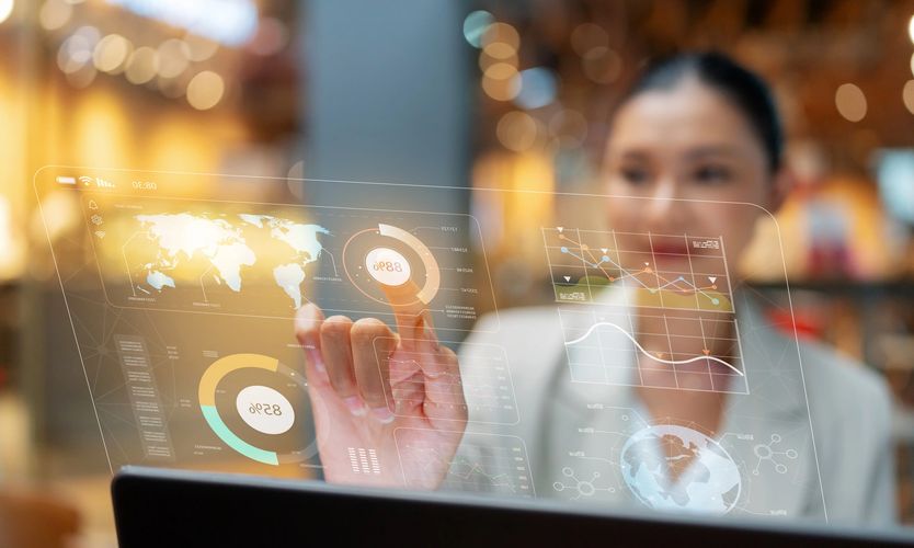 Woman interacting with futuristic transparent digital interface displaying global data and charts.