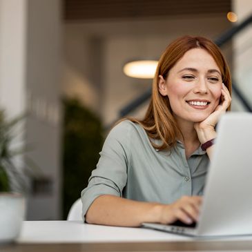 Smiling woman using a laptop in a cozy indoor setting.