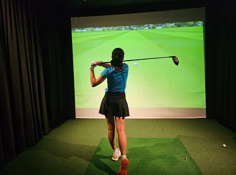 Professional female golfer holding club playing golf indoors on golf simulator