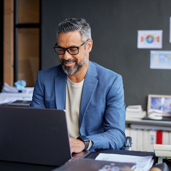 Smiling man in glasses working on a laptop in a modern office.