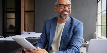 Smiling man in glasses holding a tablet in an office.