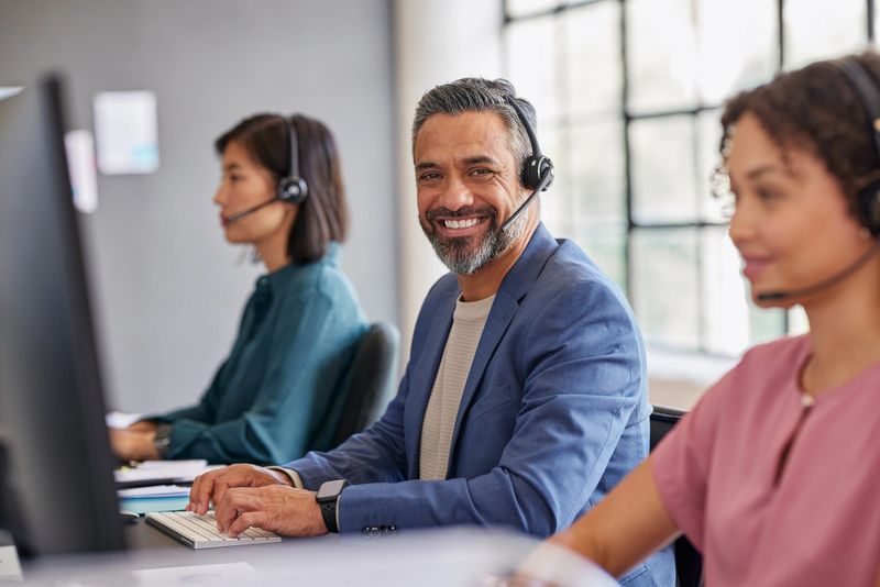 Smiling middle eastern customer support team working with headsets in a modern office. Portrait of indian mid adult call center agent providing excellent service. Multiethnic team in a customer support role, ready to assist clients.