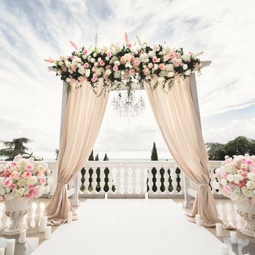 Elegant wedding arch with soft drapes and floral arrangements under a chandelier.