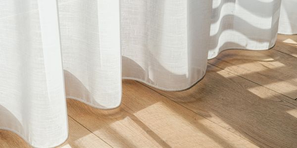 White curtains casting shadows on wooden floor in sunlight.