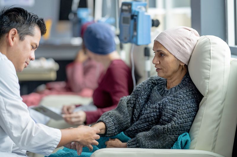 A small group of women who are battling cancer, are seen sitting in treatment chairs in an Oncology clinic.  They are each dressed comfortably, and have head scarves on to keep warm as they receive their Chemotherapy treatment.