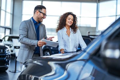 Salesman showing a woman a car in a dealership.