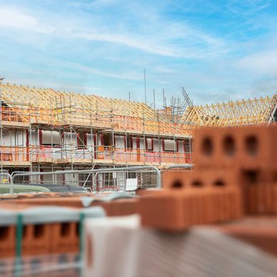 Construction site with wooden roof frames and bricks in the foreground.