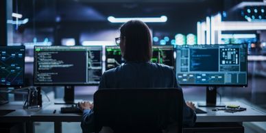 Person coding at a computer with multiple monitors in a dark room.