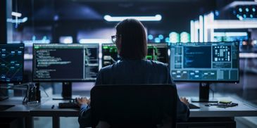 Person working on multiple computer screens with code at night.