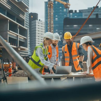 Construction workers discussing plans on a laptop at a building site.