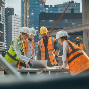Construction team reviewing plans on a laptop at an urban site.