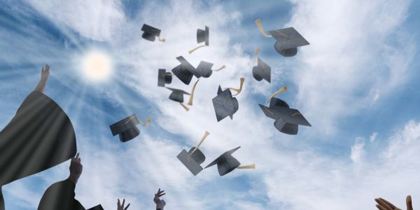 Graduates toss their caps into the air against a blue sky.