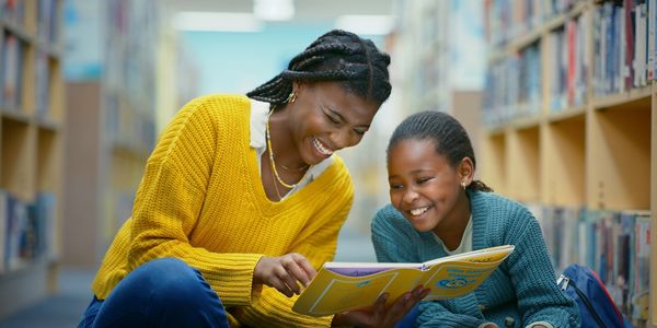 A joyful woman and girl reading a book together in a library.