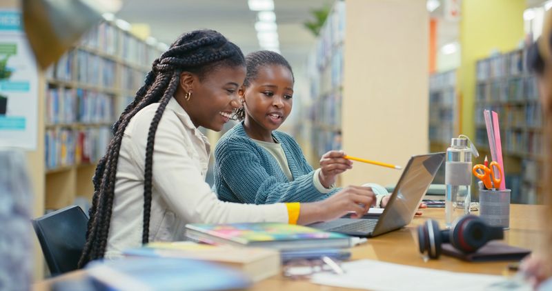 Teacher, girl and laptop for e learning in library with education support, information and advice. Woman, student and online research with studying, assessment and scholarship application for tuition