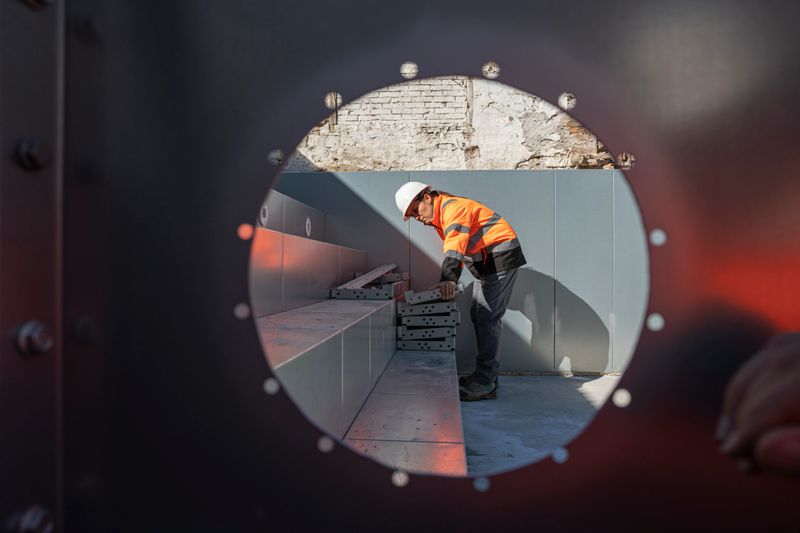 Circle framing view of female engineer in safety gear & hardhat inspecting large metal swimming pool structure on construction site during the building process.